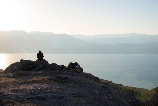 A man sits on a high mountain cliff and overlooks the horizon. A concept for hope, peace, power, soul searching. Desert mountains against the backdrop of the Red Sea. Shlomo mountain, Eilat Israel