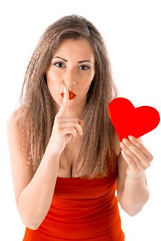 Young girl with red heart in her hand, holding her finger to her lips in a gesture for silence. Secret, silent and shush. Valentine's Day concept