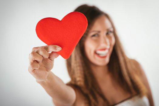 Close-up of a beautiful smiling girl holding a red heart. Selective focus. Focus on foreground, on the heart.