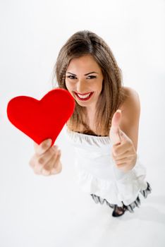 Close-up of a beautiful smiling girl holding a red heart with tumb up. Selective focus. 
