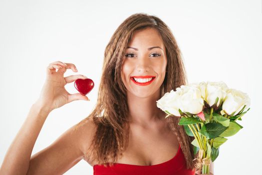 Portrait of a beautiful smiling girl holding a red heart and bouquet of white roses. Looking at camera.