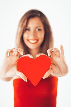 Beautiful smiling girl holding a red heart. Selective focus. Focus on the heart, on foreground.