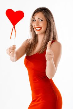 Beautiful cheerful girl standing and holding red heart and thumb up. Looking at camera.