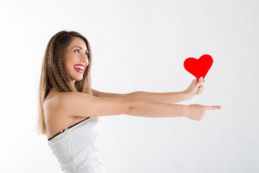 Beautiful cheerful girl standing, holding red heart and pointing something.