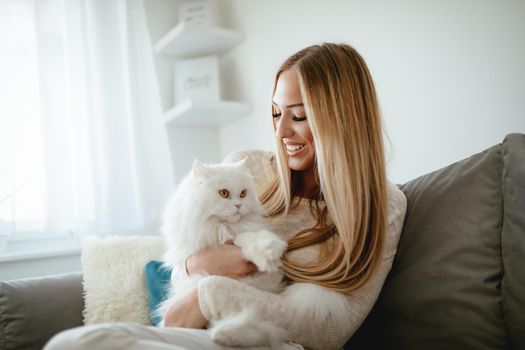 Cute young woman relaxing at the home and holding her beautiful white Persian cat.