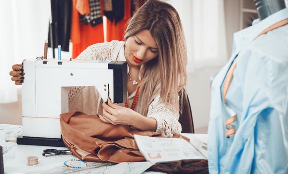 Young beautiful girl sew with a sewing machine. In the background you can see hanging garments.