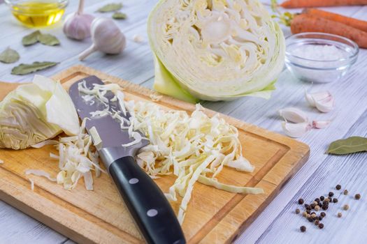 Close-up of a kitchen workspace with the process of shredding white cabbage and the ingredients for its fermentation or cooking