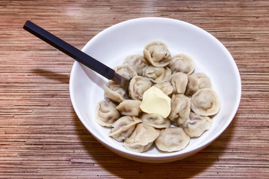 plate with homemade Russian dumplings on a wooden table and a spoon next to it.