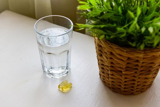 Omega-3, spirulina, chlorophyll capsules and glass of water on white wooden table. Dietary supplements, biologically active additives. vitamin pills. Health support.