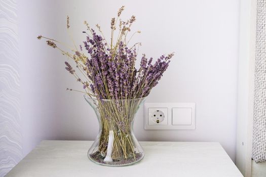 Stylish wooden bedside table and glass vase with dried lavender on it. Interior details.