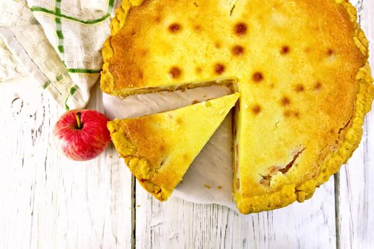 Apple pie with sour cream sauce on a parchment, fruit and napkin on a wooden plank background