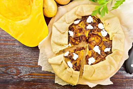 Pie of pumpkin, fried onions and soft cheese on parchment, napkin, parsley on a wooden board background from above