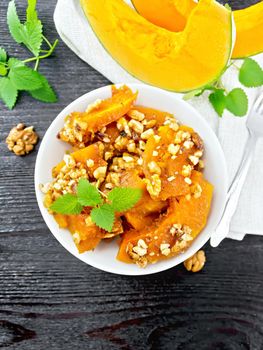 Pumpkin with walnuts and honey in a bowl, napkin and mint on a black wooden board background from above