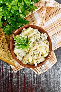 Salad with squid, egg and mushrooms in a bowl on a napkin, bread, fork and parsley on dark wooden board background from above