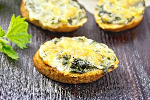 Hot sandwiches with nettles and cheese on slices of wheat bread, garlic and vegetable oil on a wooden board background
