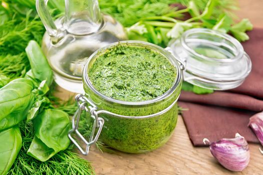 Sauce of dill, parsley, basil, cilantro, other spicy herbs, garlic and vegetable oil in a glass jar, a towel on wooden board background