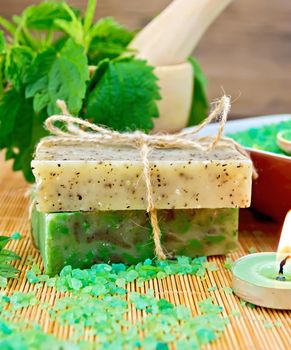 Two bars of homemade soap with twine, bath salt, nettle in a mortar, scented candle on a wooden boards background