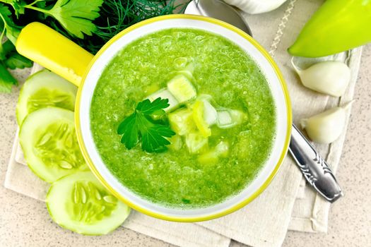 Cucumber soup with green peppers and garlic in a yellow bowl, parsley on a background of a granite table top