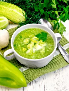 Cucumber soup with green peppers and garlic in a white bowl on a napkin, parsley on a wooden boards background