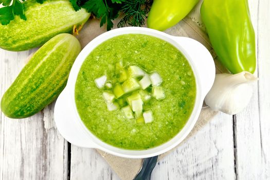 Cucumber soup with green peppers and garlic in a bowl on a napkin, parsley on a background of wooden boards on top