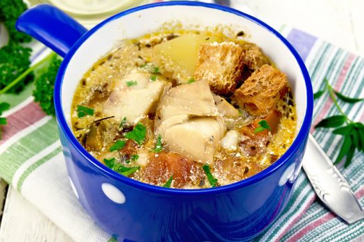 Fish soup with tomatoes, potatoes, peppers, croutons and cream in a blue bowl on a napkin, parsley on a light wooden board background