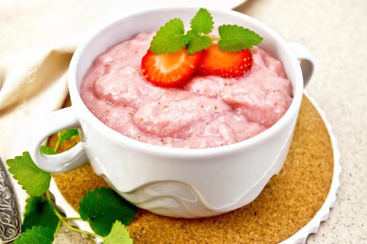 Strawberry soup with berries and mint in a bowl on a stand, a towel and a spoon on a background of stone table