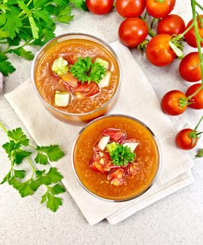 Gazpacho tomato soup in two glasses with parsley and vegetables on a napkin against the background of the stone table top