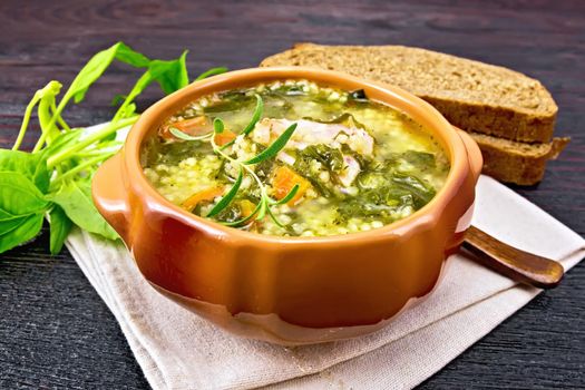 Pork ribs soup with couscous and spinach in a clay bowl on napkin, bread on wooden board background