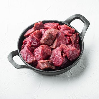 Raw ingredients for goulash. Fresh raw chopped beef set, in cast iron frying pan, on white stone surface, square format