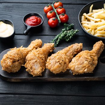 Fried crispy chicken legs, drumstick parts on black wooden table.