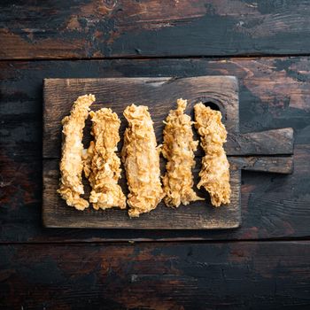 Crispy chicken sticks meat on dark wooden background, top view.