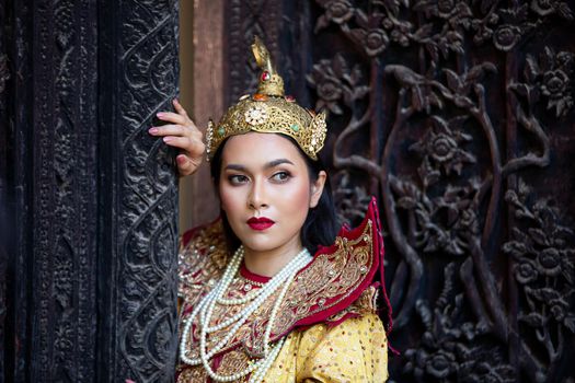 Portrait of an Asian Women in Mandalay, Myanmar Woman with golden Traditional Clothes are Standing Against Art Carving Wooden Door.