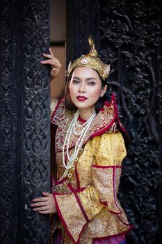 Portrait of an Asian Women in Mandalay, Myanmar Woman with golden Traditional Clothes are Standing Against Art Carving Wooden Door.