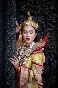 Portrait of an Asian Women in Mandalay, Myanmar Woman with golden Traditional Clothes are Standing Against Art Carving Wooden Door.