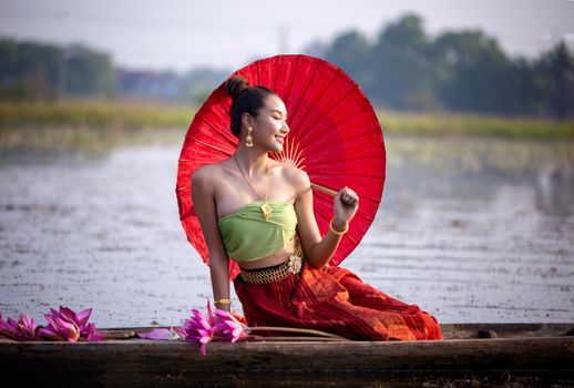 Young Asian women in Traditional dress in the boat and pink lotus flowers in the pond.Beautiful girls in traditional costume.Thai. Ayutthaya, elegance.