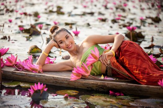 Young Asian women in Traditional dress in the boat and pink lotus flowers in the pond.Beautiful girls in traditional costume.Thai. Ayutthaya, elegance.