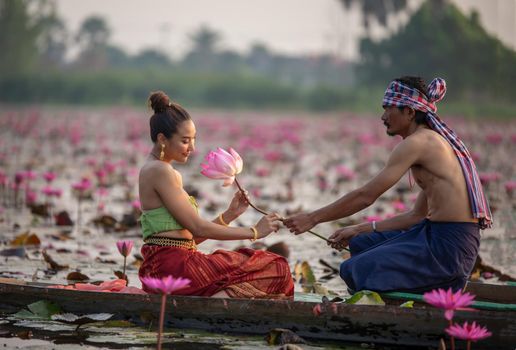 Young Asian women in Traditional dress in the boat and pink lotus flowers in the pond.Beautiful girls in traditional costume.Thai. Ayutthaya, elegance.