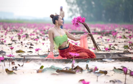 Young Asian women in Traditional dress in the boat and pink lotus flowers in the pond.Beautiful girls in traditional costume.Thai. Ayutthaya, elegance.