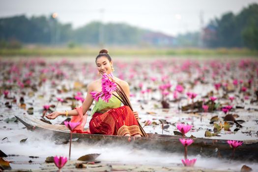 Young Asian women in Traditional dress in the boat and pink lotus flowers in the pond.Beautiful girls in traditional costume.Thai. Ayutthaya, elegance.