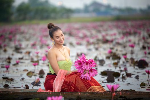 Young Asian women in Traditional dress in the boat and pink lotus flowers in the pond.Beautiful girls in traditional costume.Thai. Ayutthaya, elegance.