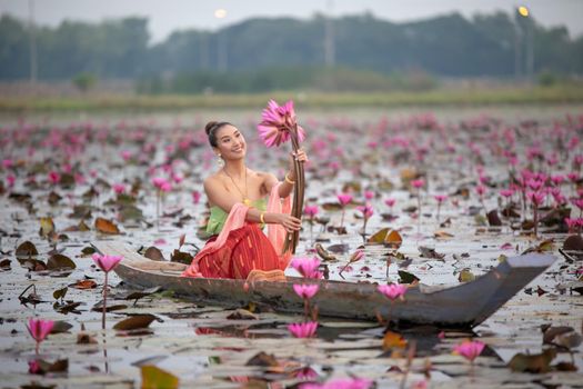 Young Asian women in Traditional dress in the boat and pink lotus flowers in the pond.Beautiful girls in traditional costume.Thai. Ayutthaya, elegance.