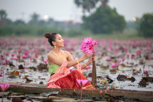 Young Asian women in Traditional dress in the boat and pink lotus flowers in the pond.Beautiful girls in traditional costume.Thai. Ayutthaya, elegance.