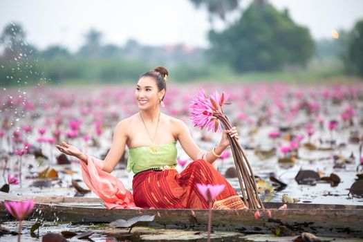 Young Asian women in Traditional dress in the boat and pink lotus flowers in the pond.Beautiful girls in traditional costume.Thai. Ayutthaya, elegance.