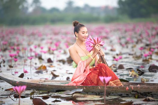 Young Asian women in Traditional dress in the boat and pink lotus flowers in the pond.Beautiful girls in traditional costume.Thai. Ayutthaya, elegance.