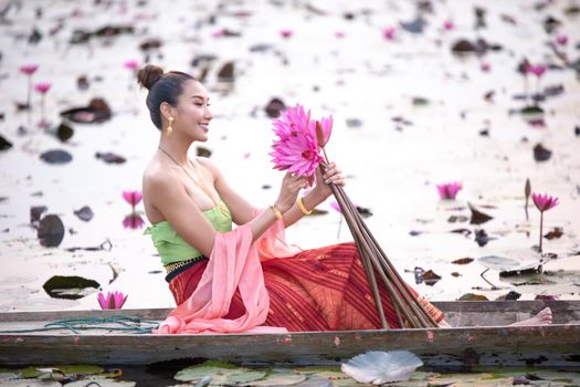 Young Asian women in Traditional dress in the boat and pink lotus flowers in the pond.Beautiful girls in traditional costume.Thai. Ayutthaya, elegance.