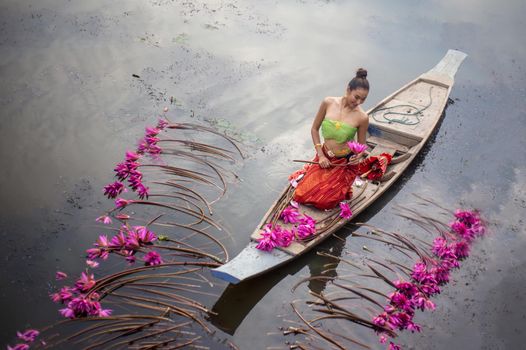 Young Asian women in Traditional dress in the boat and pink lotus flowers in the pond.Beautiful girls in traditional costume.Thai. Ayutthaya, elegance.