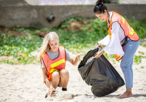 Green volunteering. Optimistic two volunteers holding garbage bag and help picking up trash at park, they're picking up the garbage and putting it in a black garbage bag. ecology protection concept.