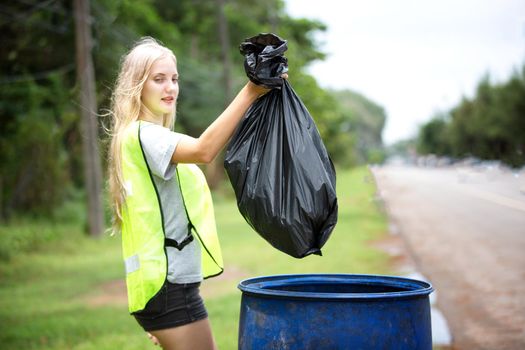 Green volunteering. Optimistic two volunteers holding garbage bag and help picking up trash at park, they're picking up the garbage and putting it in a black garbage bag. ecology protection concept.