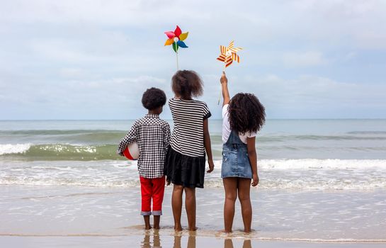 Kids playing running on sand at the beach, A group of children holding hands in a row on the beach in summer, rear view against sea and blue sky