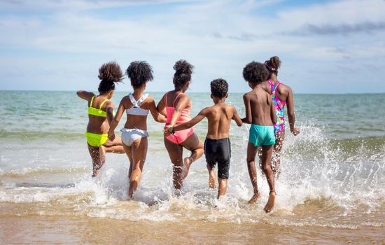 Kids playing running on sand at the beach, A group of children holding hands in a row on the beach in summer, rear view against sea and blue sky